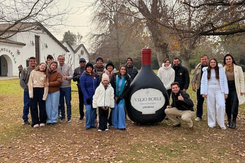 A group of people posing with a large bottle labeled 'VIEJO ROBLE' in a park with a church in the background. 4
