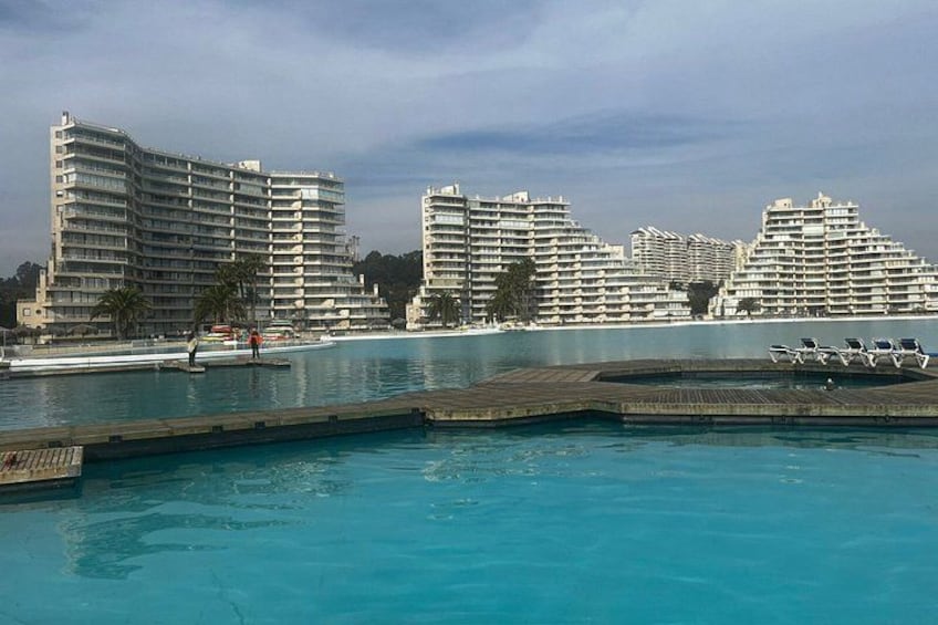 A large swimming pool with a wooden deck, surrounded by high-rise buildings. 2