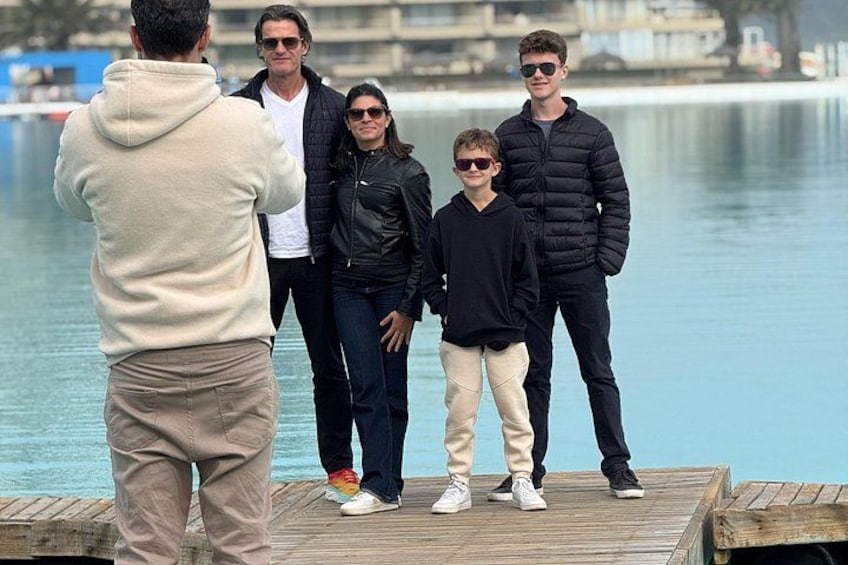 A group of people standing on a wooden dock by a calm body of water. 3
