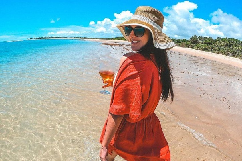 A person in a red dress and straw hat standing on a beach with clear water and a distant shoreline. 4