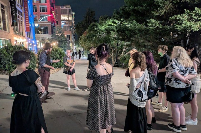A group of people standing outdoors at night, engaged in conversation. 1