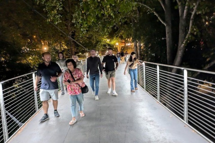 A pedestrian bridge with people walking, surrounded by trees and lights. 2
