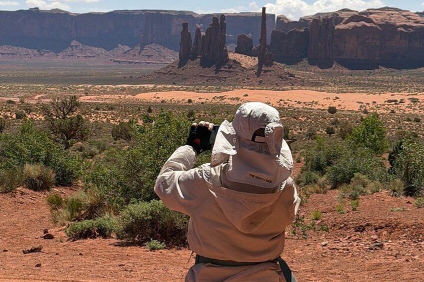 A person in a white suit taking a photo of a desert landscape with rock formations. 2