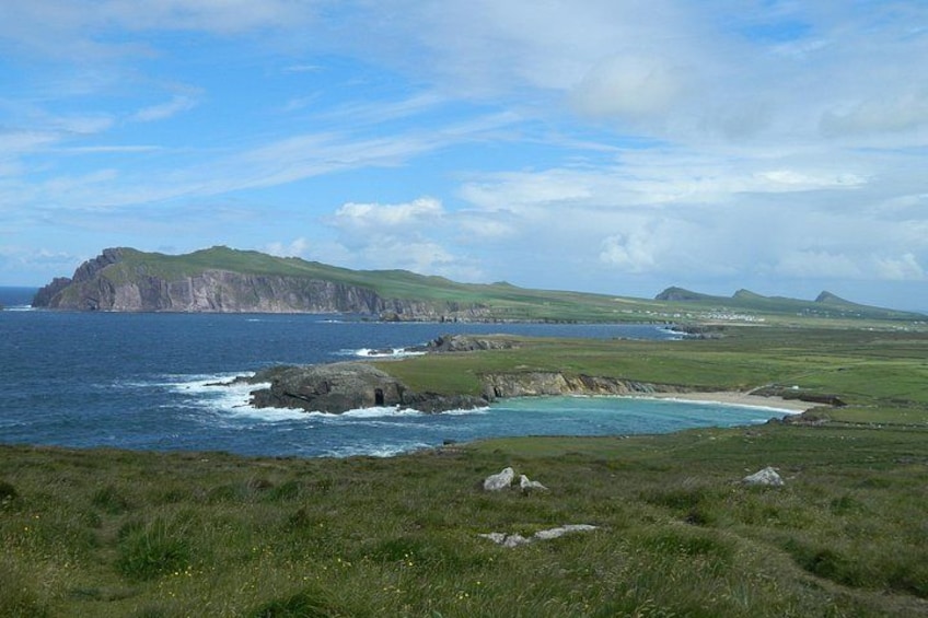 A coastal landscape with grassy terrain, a rocky shoreline, and a prominent hill in the distance. 3