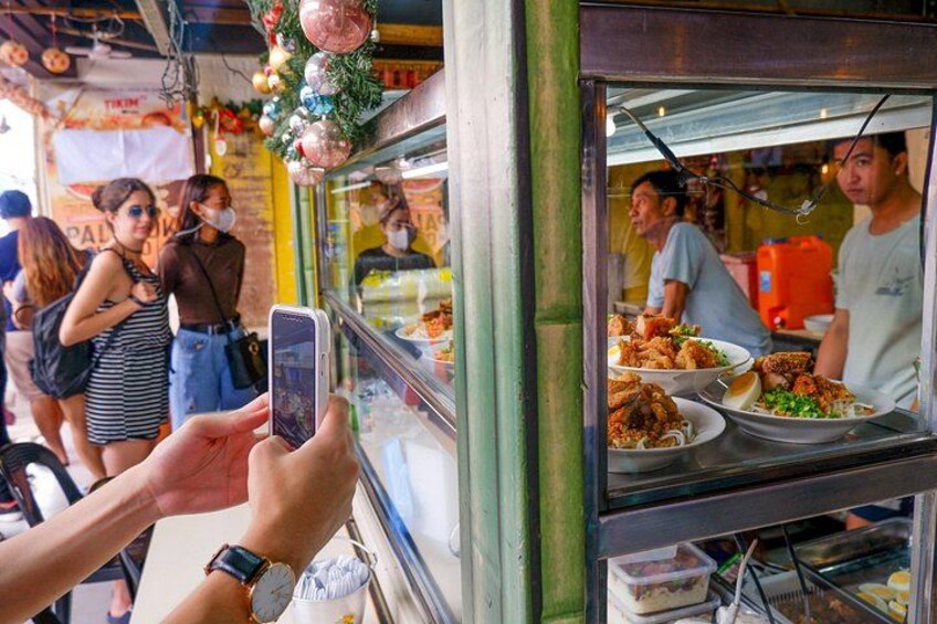 Una bancarella di cibo con una persona che scatta una foto, un bancone pieno di prelibatezze e una decorazione festosa. 2