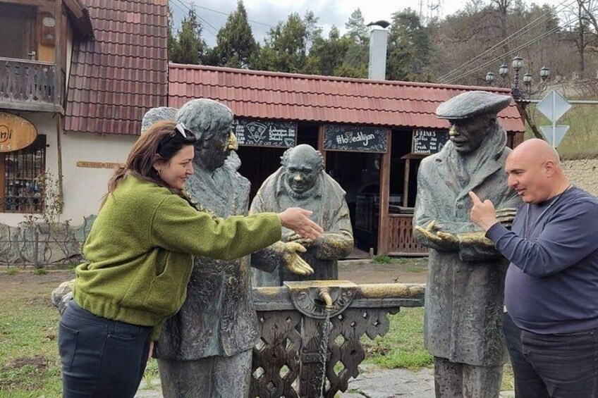 A woman interacting with a statue, a man gesturing, and a building with a red roof in the background. 3