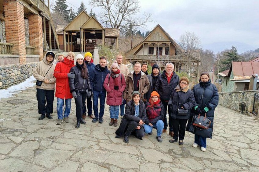 A group of people posing in front of a rustic building with stone steps and a wooden structure in the background. 5