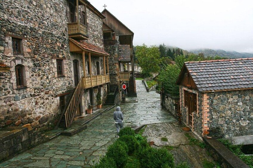 A narrow stone pathway between buildings, a person walking, and a red circular sign. 1