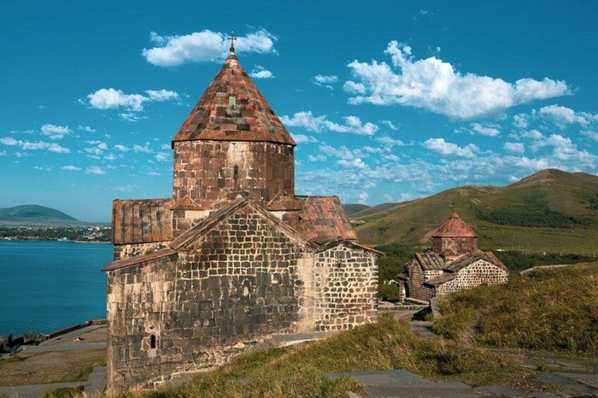 A historic stone church with a bell tower, surrounded by grassy hills and a body of water. 4