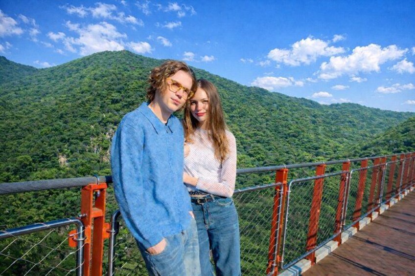 A wooden bridge with red railings, surrounded by lush green mountains. 4