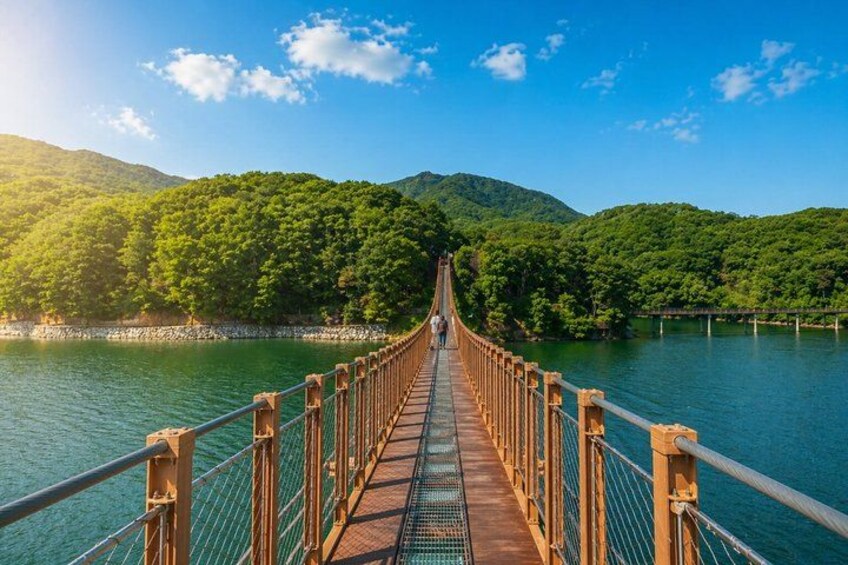 Un puente colgante de madera sobre un río, con colinas verdes y exuberantes al fondo. 2