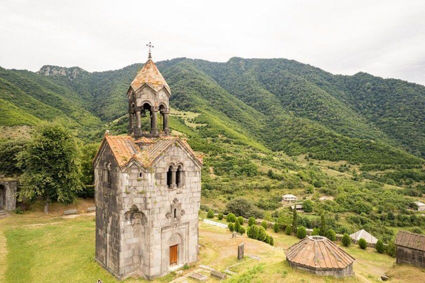 A stone church with a bell tower, surrounded by lush green hills and a small village. 4