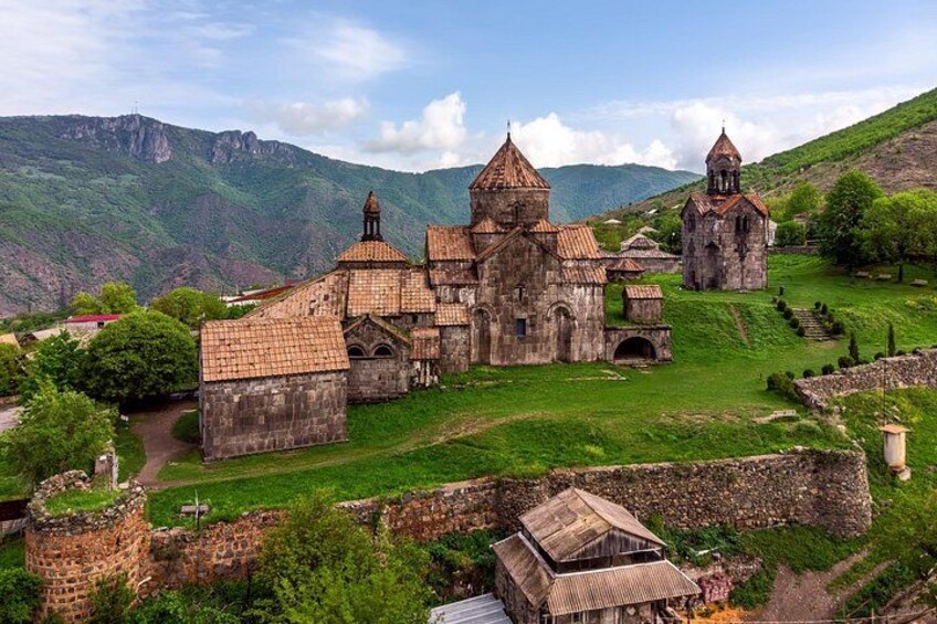 A historic church complex with multiple buildings, surrounded by lush green hills and a clear sky. 2