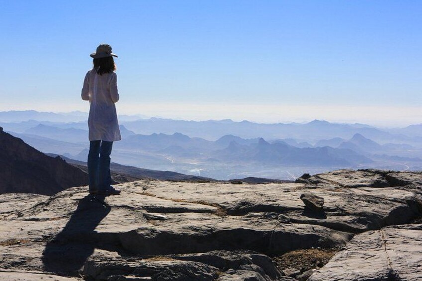 A person standing on rocky terrain overlooking a mountainous landscape. 2