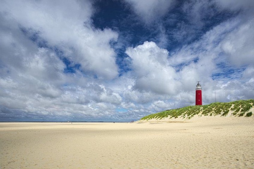 A red lighthouse on a sandy beach with a cloudy sky. 1