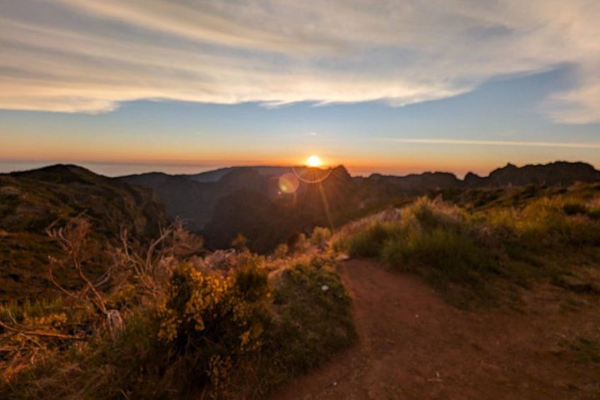 A sunset over a mountainous landscape with a dirt path leading through the terrain. 4
