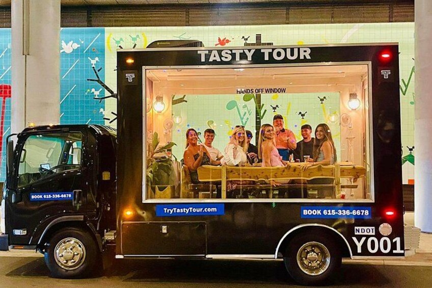Un food truck nero con un cartello che recita 'Tasty Tour' e un gruppo di persone all'interno. 4