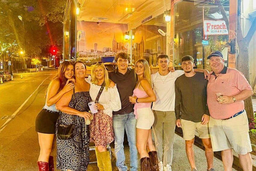 Un gruppo di persone in piedi su un marciapiede di notte, con una strada cittadina e un ristorante francese sullo sfondo. 5