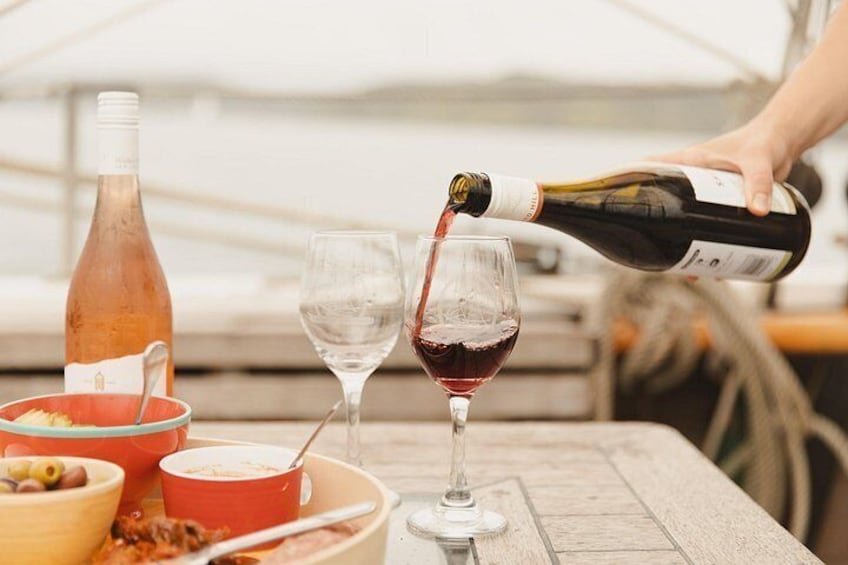 A person pouring wine into a glass, a bottle of rosé wine, and a bowl of food on a table. 5