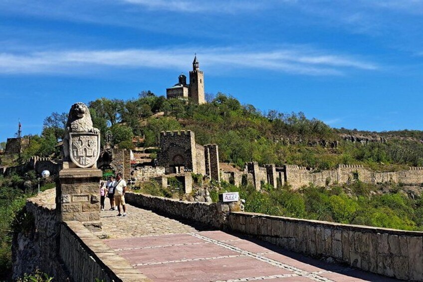 Un puente de piedra con una estatua de león, un castillo en una colina y un cielo azul despejado. 3
