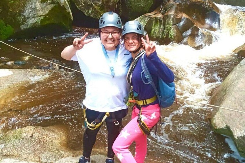 Two people rappelling down a rocky river with flowing water. 4