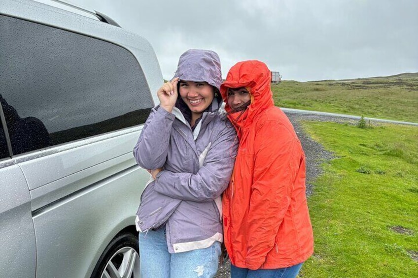 Two people standing beside a silver car on a grassy roadside. 5