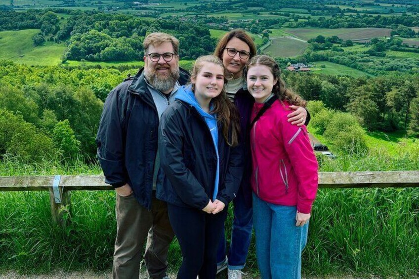 A group of people standing on a grassy hill with a scenic view of rolling hills and a river in the distance. 4