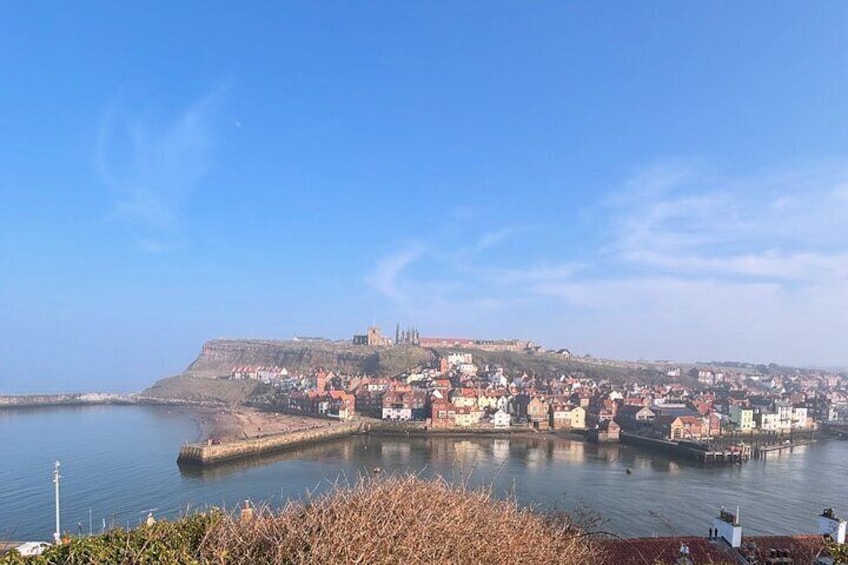 A coastal town with a prominent fort on a hill, calm waters, and a clear sky. 3
