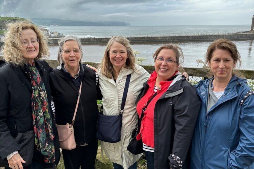 A group of people standing by a waterfront with a stone wall and a view of the sea. 2