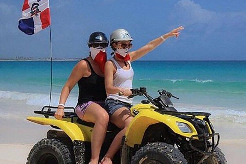 Two people on a yellow ATV on a beach with a flag. 3