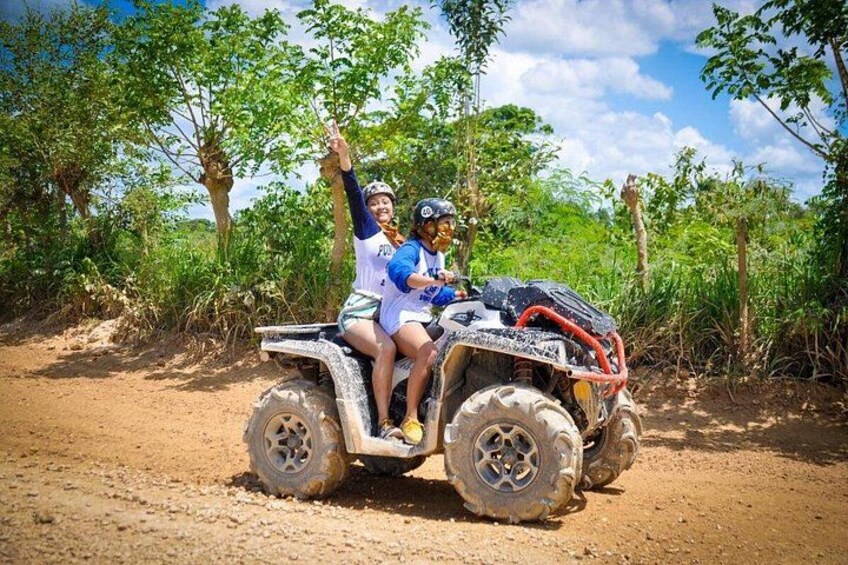 Two people on an ATV in a dirt path surrounded by greenery. 2