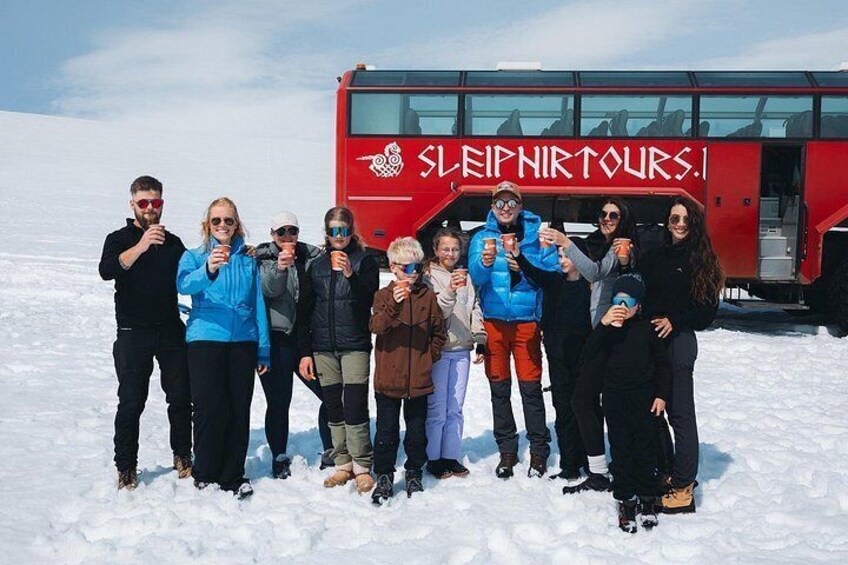 Un groupe de personnes pose devant un autobus rouge sur lequel on peut lire l’inscription « SLEIPNIRTOURS.I. », et elles se tiennent sur un sol recouvert de neige. 2
