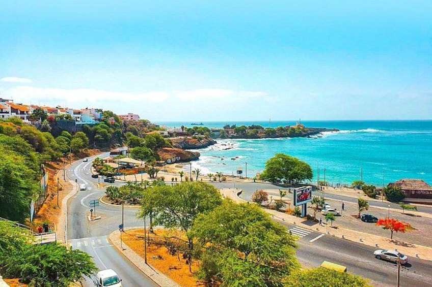 A coastal town with a winding road, a beach, and a clear blue sea. 1