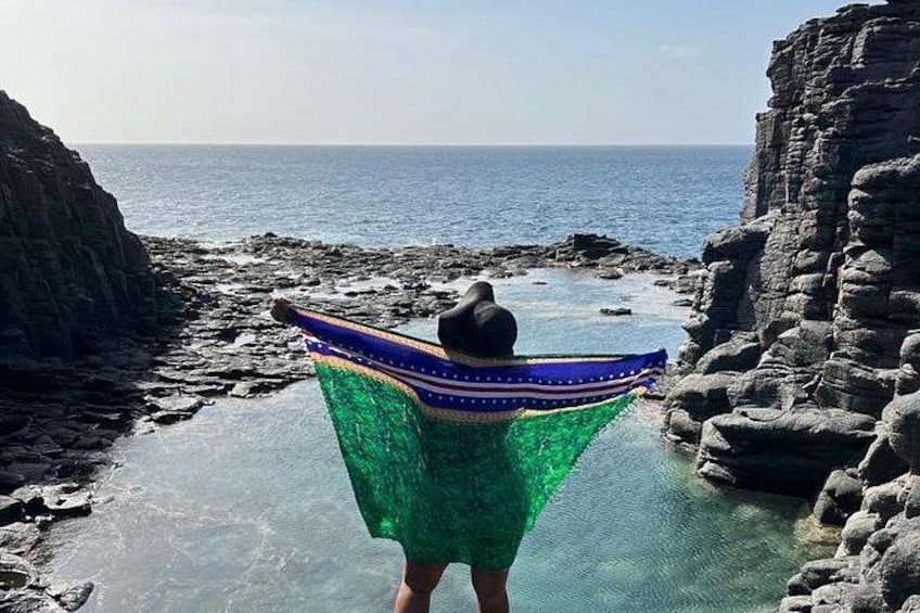 A person standing on a rocky beach with a colorful garment spread out, facing the ocean. 4