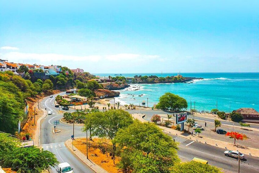 A coastal town with a winding road, a beach, and a clear blue sky. 1
