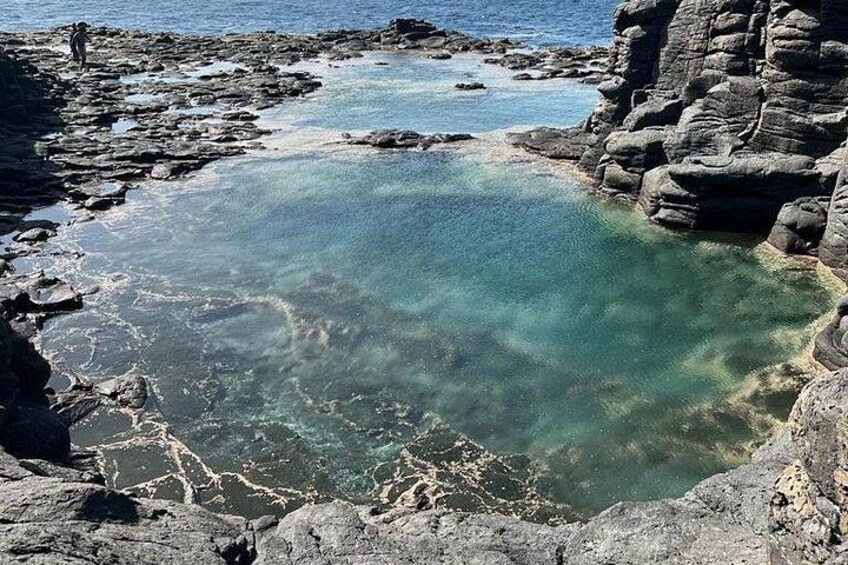 A rocky shoreline with clear water and a person standing on the rocks. 5