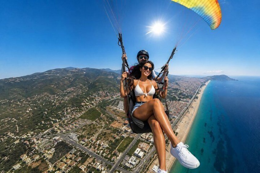 Eine Person gleitet mit einem Paragleiter über eine Küstenlandschaft bei blauem Himmel und Blick auf die darunterliegende Küste. 3