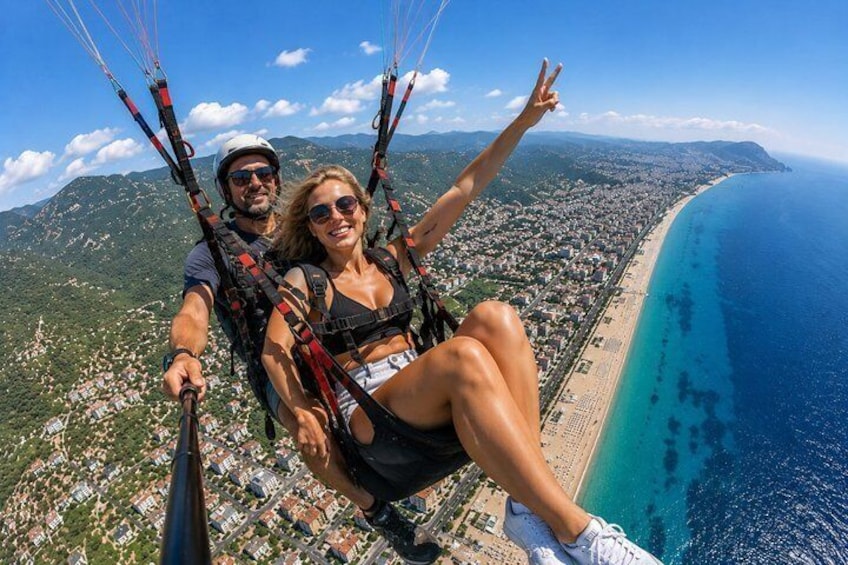 Eine Person tandemspringt mit dem Gleitschirm über einer Küstenstadt, im Hintergrund Strand und Berge. 5
