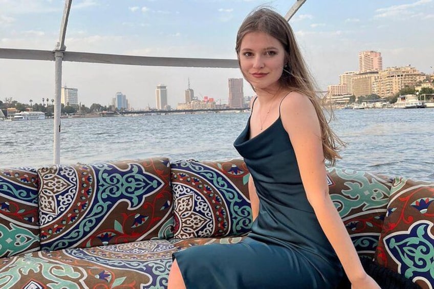 Una persona sentada en un sofá estampado frente a un cuerpo de agua, con edificios al fondo. 1