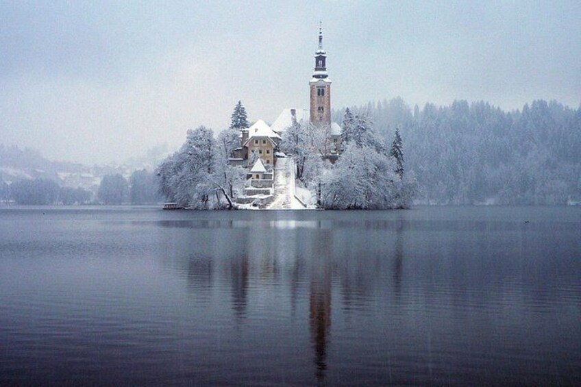 A snow-covered island with a church and a tower, surrounded by a calm lake and trees. 3