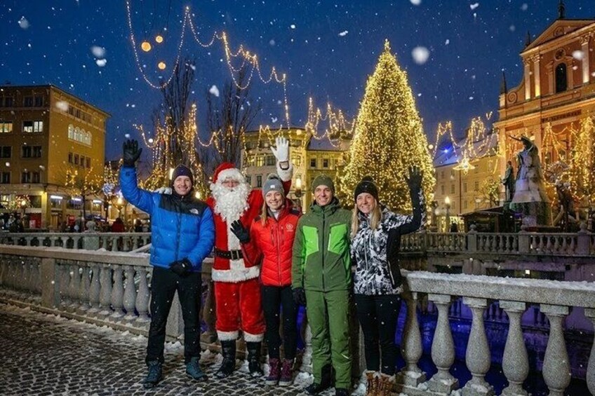 Un grupo de personas posando frente a un árbol de Navidad decorado y una estatua, mientras cae nieve. 2