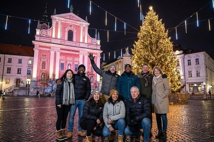 A group of people posing in front of a brightly lit pink building and a decorated Christmas tree. 5