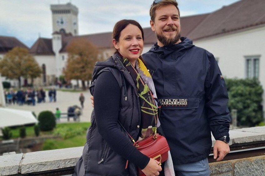 A couple standing on a stone ledge with a historic building and a tower in the background. 4