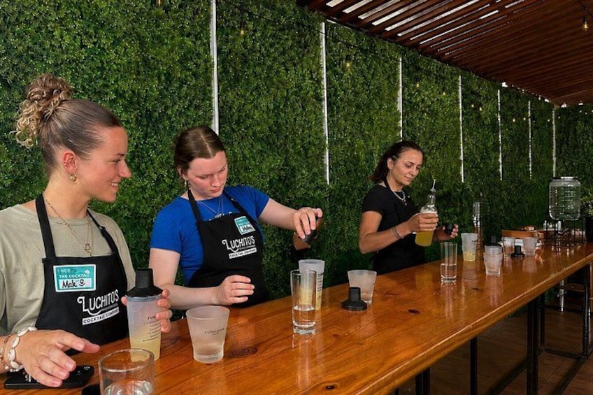 Trois personnes sont assises au comptoir d’un bar, devant des boissons, et portent des tabliers arborant la marque « Luchitos ». 3