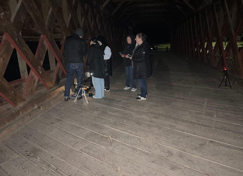 Un gruppo di persone in piedi su un ponte di legno di notte, con una macchina fotografica su un treppiede. 2