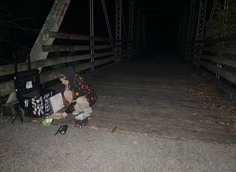 Una persona seduta a terra sotto un ponte di notte, con uno zaino e una scatola di oggetti. 4