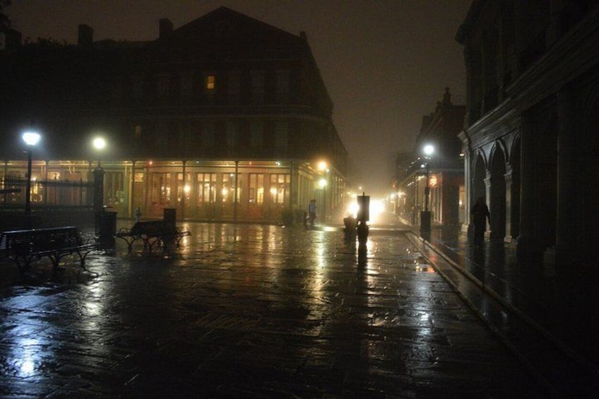 A wet cobblestone street at night with illuminated buildings and benches. 2