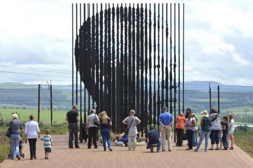 Un gruppo di persone riunite attorno a una grande scultura verticale in un campo aperto. 4