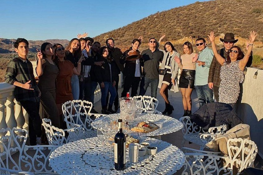 A group of people at an outdoor dining area with tables and chairs, surrounded by a mountainous landscape. 2