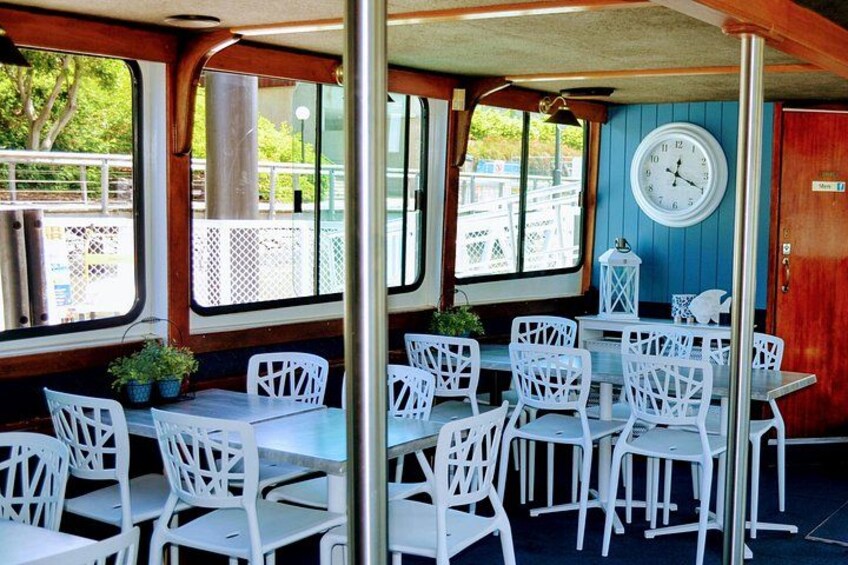 A covered outdoor seating area with white chairs and tables, a clock on the wall, and a view of the outside. 1